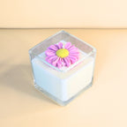 White candle in clear glass topped with a handcrafted pink flower decoration – Wicks of Intention.