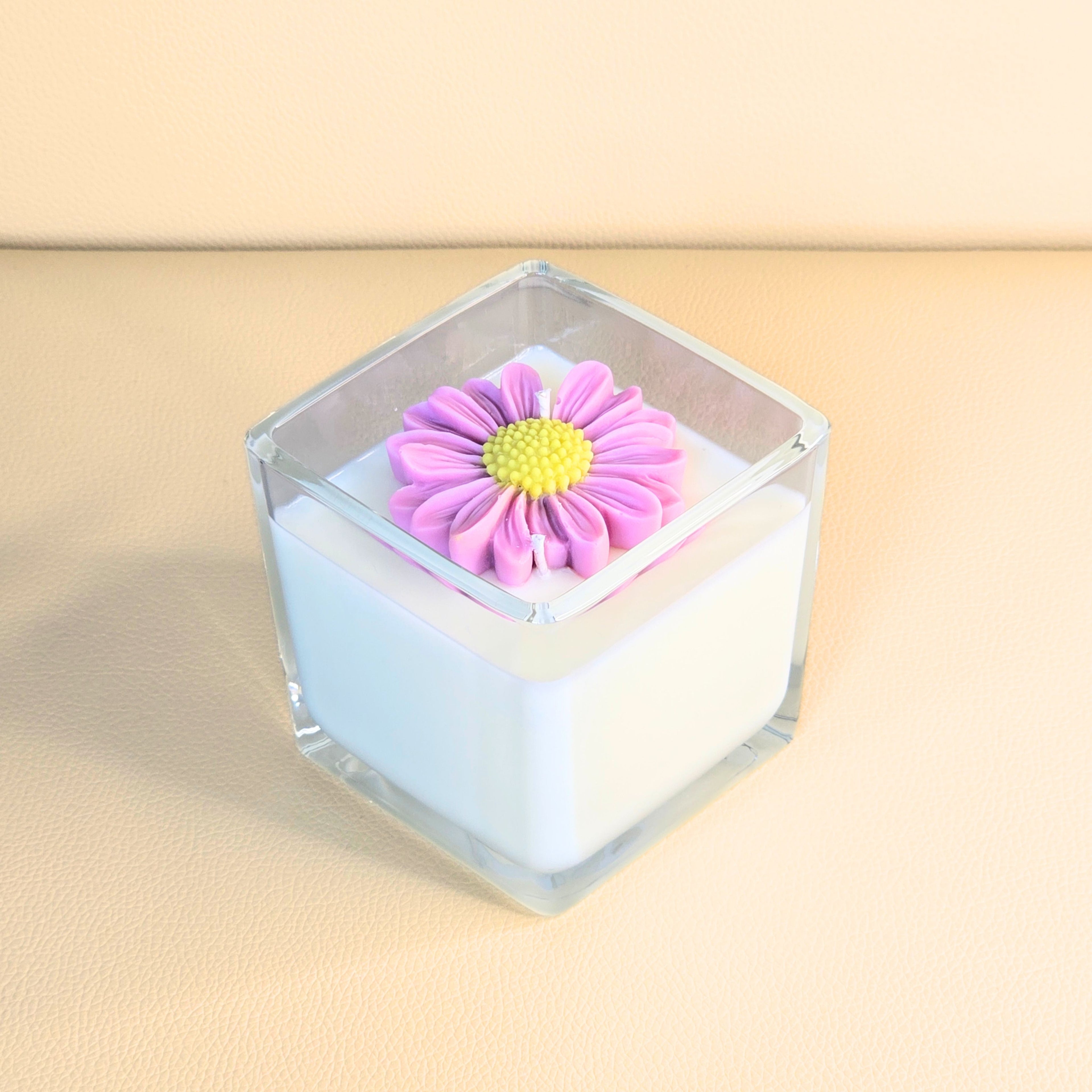 White candle in clear glass topped with a handcrafted pink flower decoration – Wicks of Intention.
