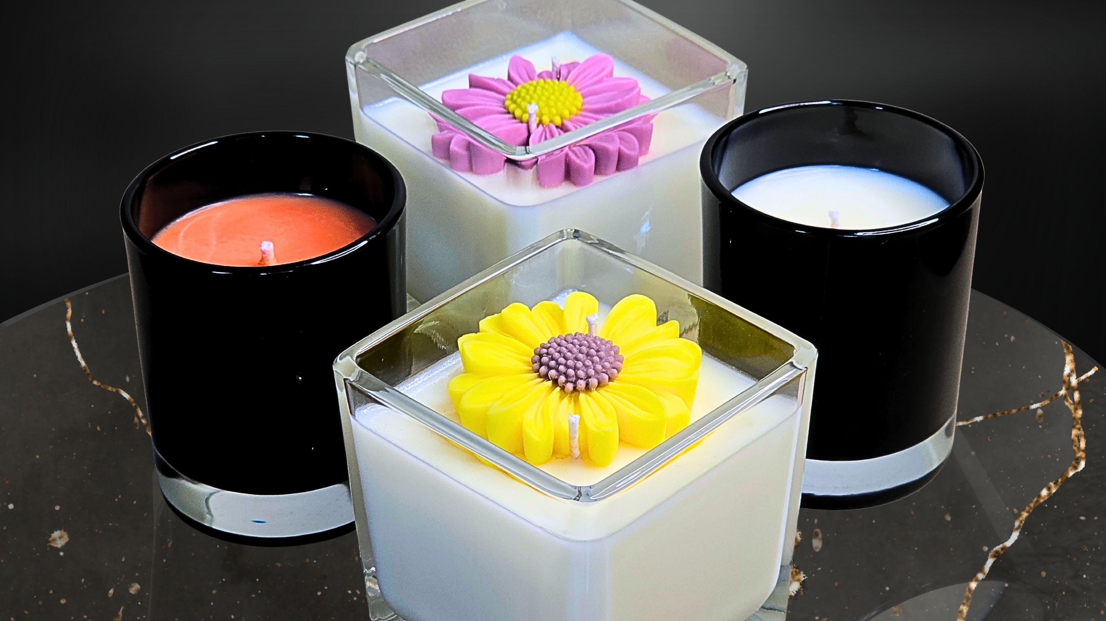 A collection of Wicks of Intention handcrafted soy candles including floral and classic designs displayed on a dark marble table.