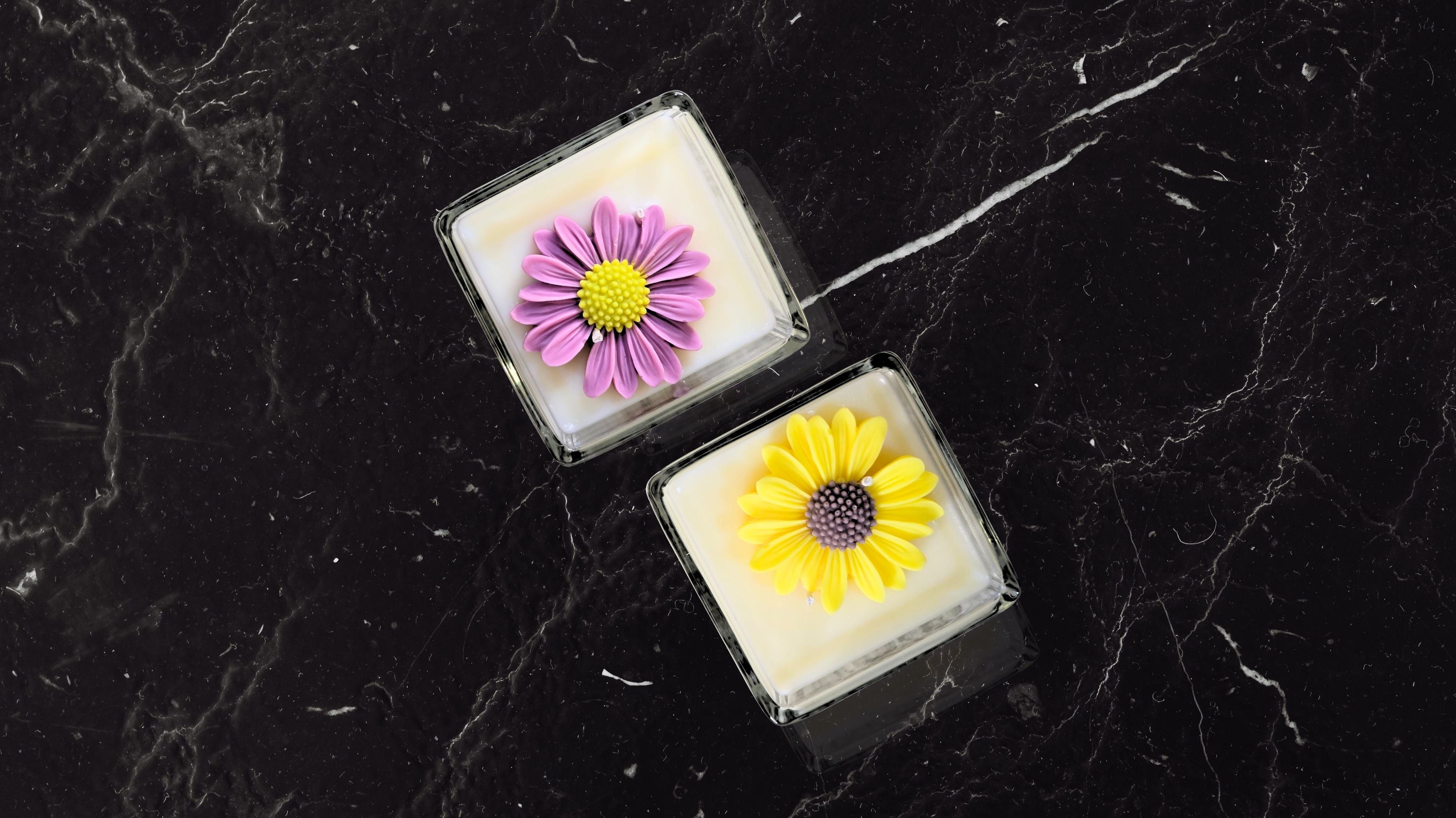 Two handcrafted soy wax candles with floral designs placed on a black marble surface enhancing the beauty of intentional rituals.